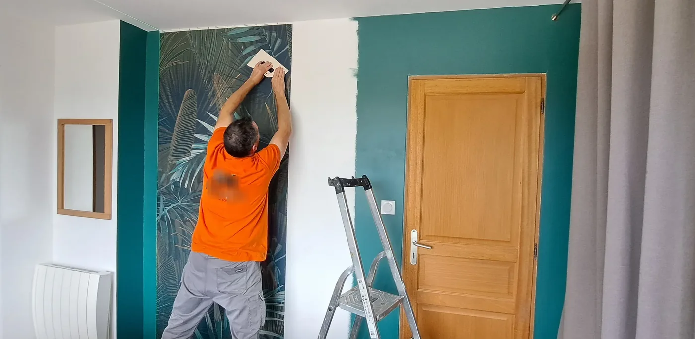 Olivier VERGÉ posant un papier peint panoramique après la mise en peinture d'une chambre